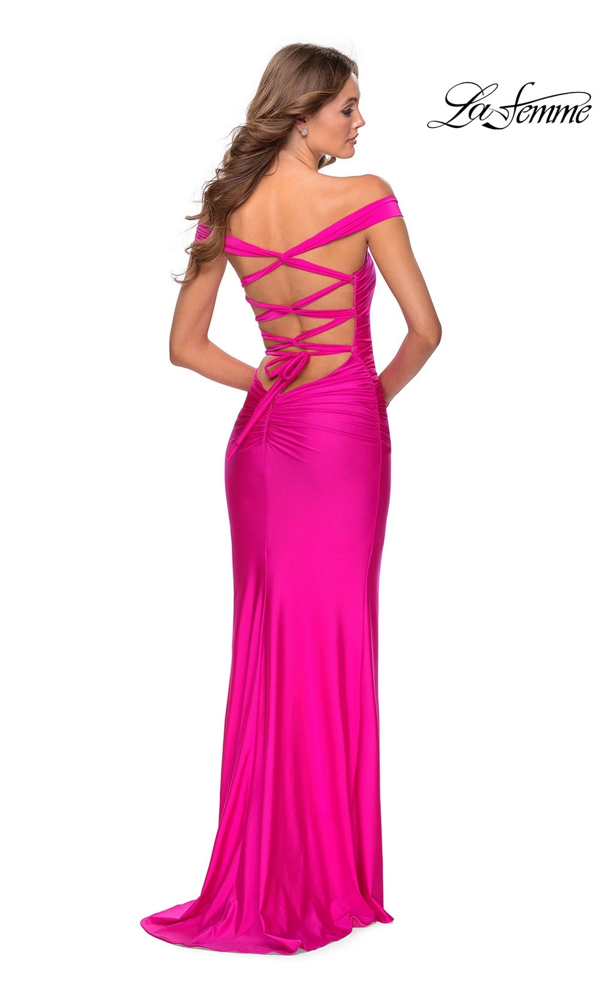 Woman in a bright pink La Femme Strappy-Back Tight Long Prom Dress 28506, featuring off-the-shoulder straps and a crisscross lace-up back, standing against a white background.